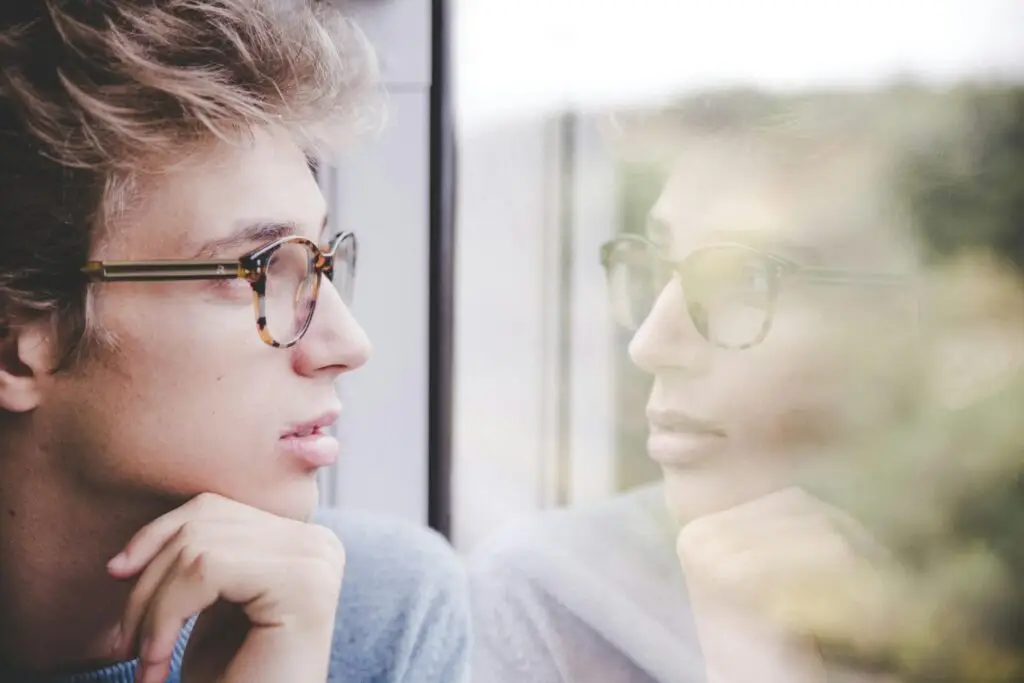 An image of a man looking at a window and seeing his reflection representing Dare 2 Share's blog Youth Lessons on Identity [3 Lessons Included]