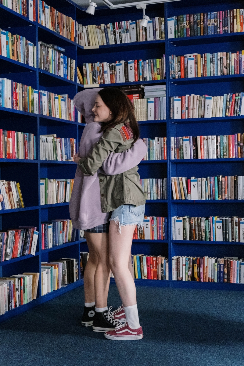 Image of two teenagers hugging in a library after one teen used evangelism to tell the other about Jesus. It represents youth leadership and how Dare 2 Share's Global Day of Evangelism will help teens share the gospel.